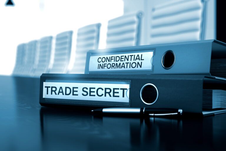 Two separate, stacked binders labeled Trade Secrets and Confidential Information respectively