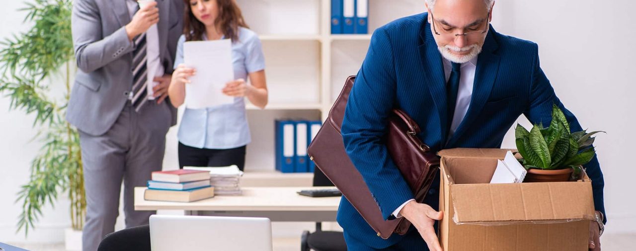 Older man picking up box off desk to leave office