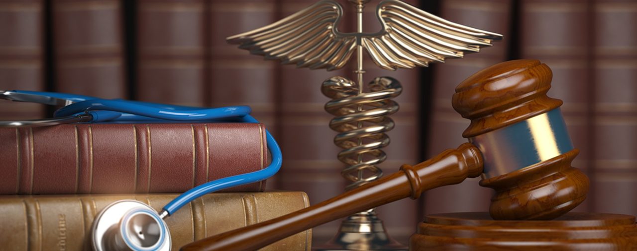 A stethoscope and a judges gavel placed on a table in front of a bookshelf. The combination signifies the overlap of medicine and law when talking about how to defend a Texas Medical Board Review