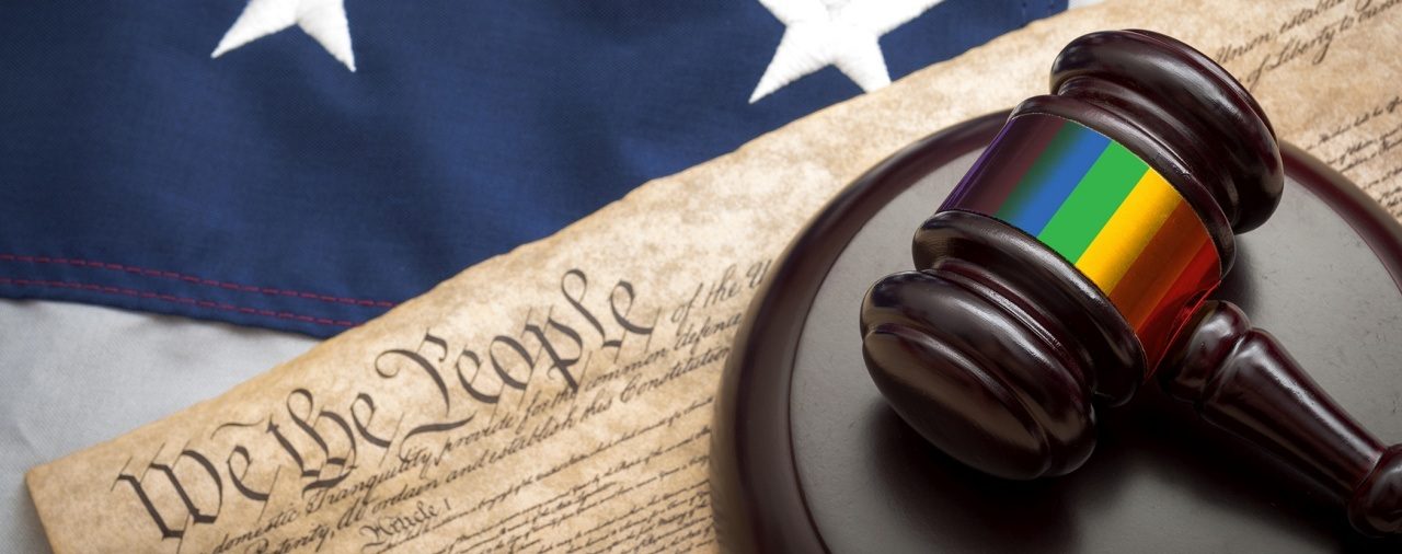 We the People parchment lying on US flag and gavel with a band in rainbow colors around the head of the gavel.