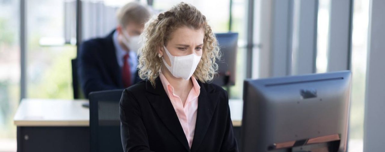 Woman at work sitting at her desk wearing a mask