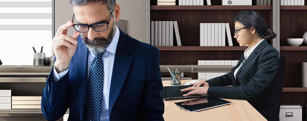 wrongful termination meeting. man in a suit looking at a paper and woman behind him on the computer. Important meeting